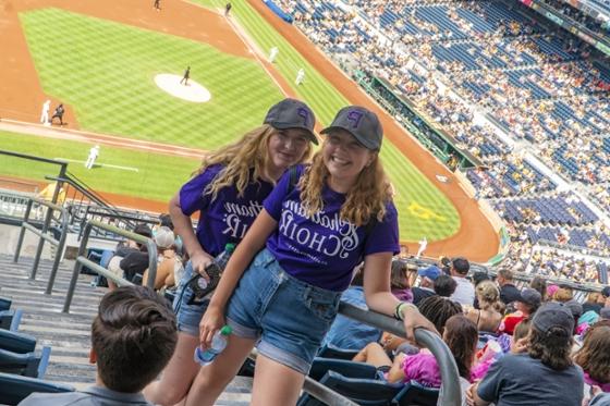  两名波胆网站唱诗班的女学生穿着相配的紫色t恤，在匹兹堡海盗队的比赛中合影.